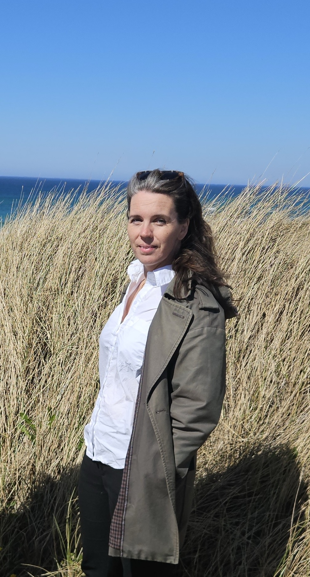Sisilie, grunnlegger av Hjem med oss, i mørk jakke og hvit skjorte ved havet